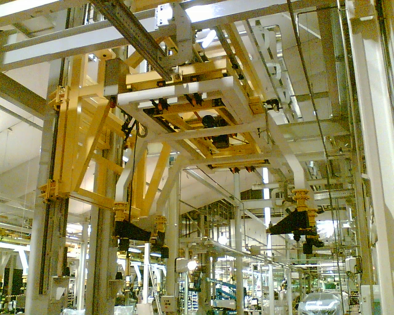 Vista ravvicinata di un sistema di trasporto aereo giallo con telai sospesi per la movimentazione automatizzata di carrozzerie.