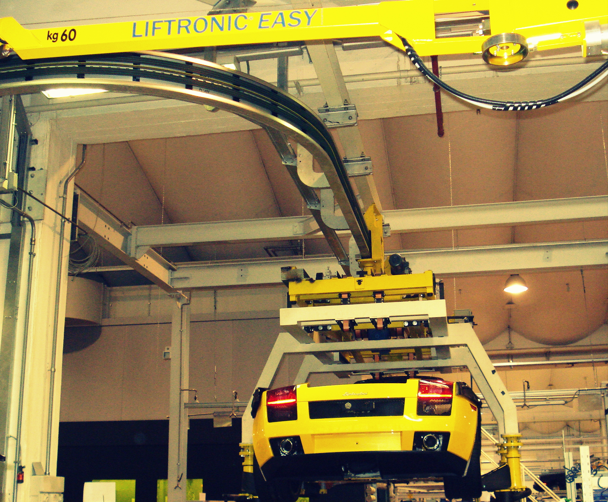 Telaio giallo di supporto con sistema “Liftronic Easy” da 60 kg che movimenta una Lamborghini gialla lungo la linea di produzione.