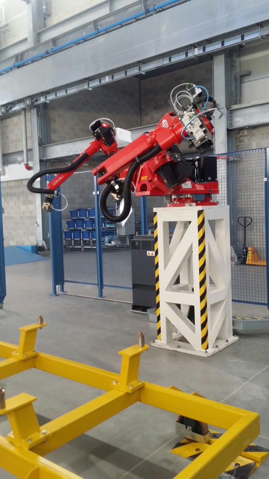 Primo piano di un robot Comau rosso installato su supporto rialzato bianco e giallo, progettato per operazioni di manipolazione.