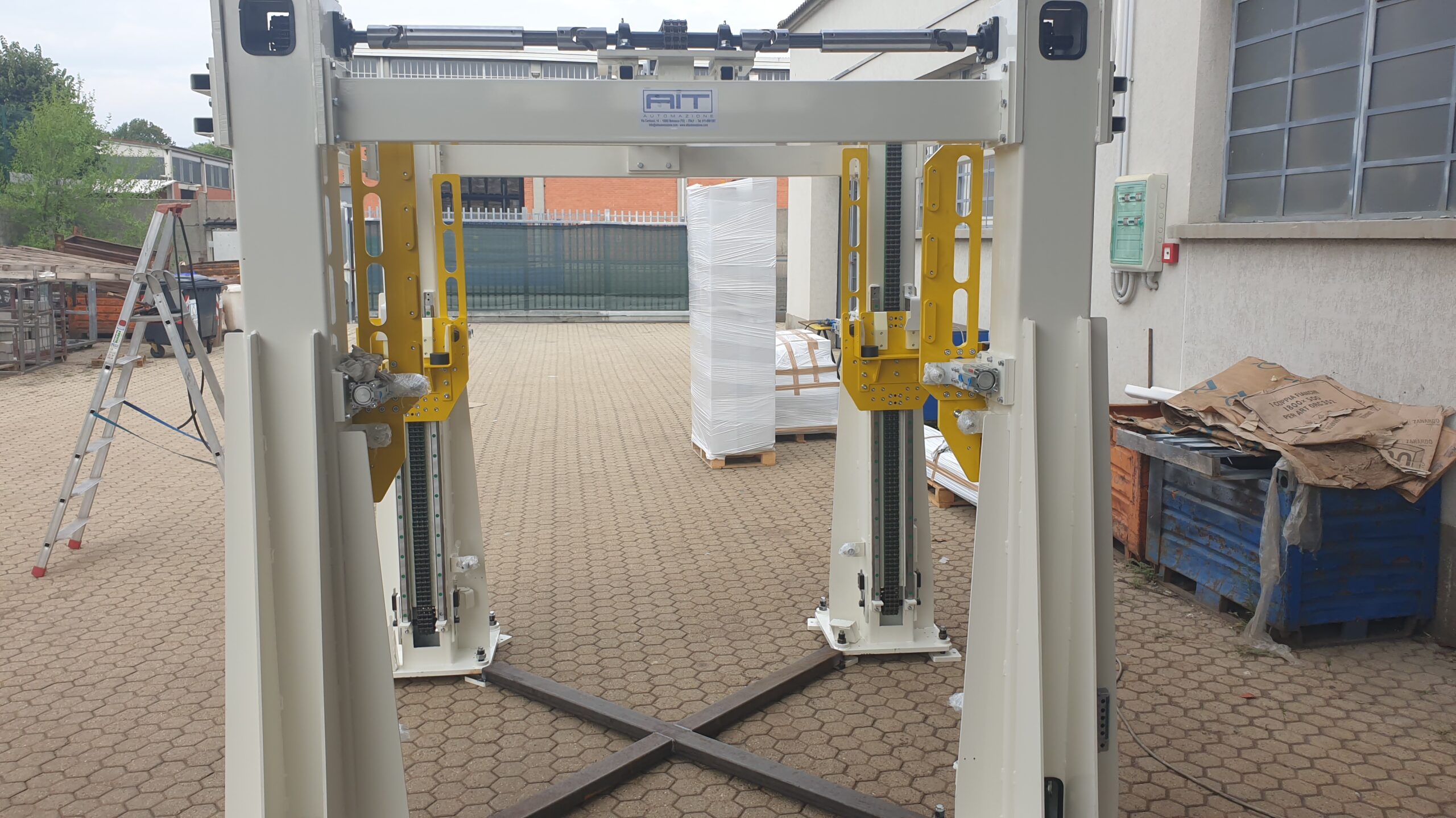 Struttura metallica bianca con elementi gialli e logo AIT Automazione, posizionata in esterno su pavimentazione industriale.