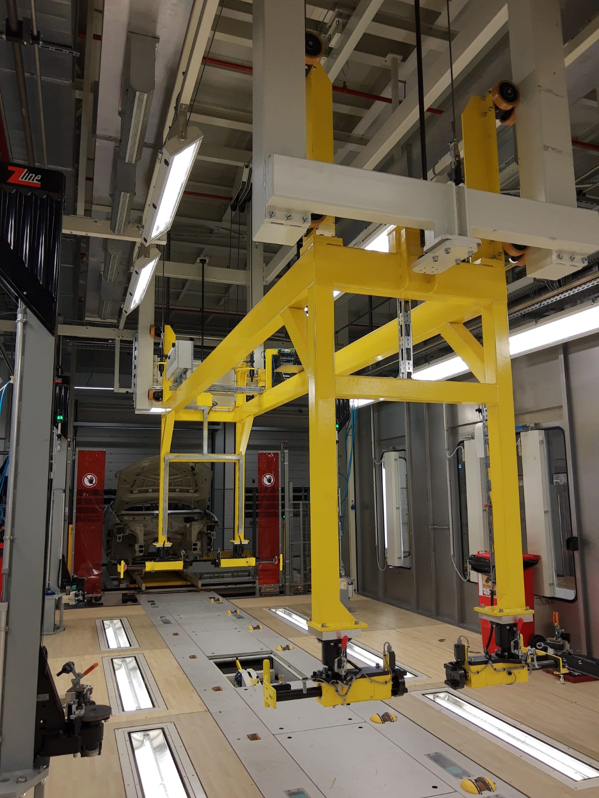 Impianto di sollevamento carrozzerie auto con struttura gialla e sistemi di fissaggio, all’interno di linea produttiva.