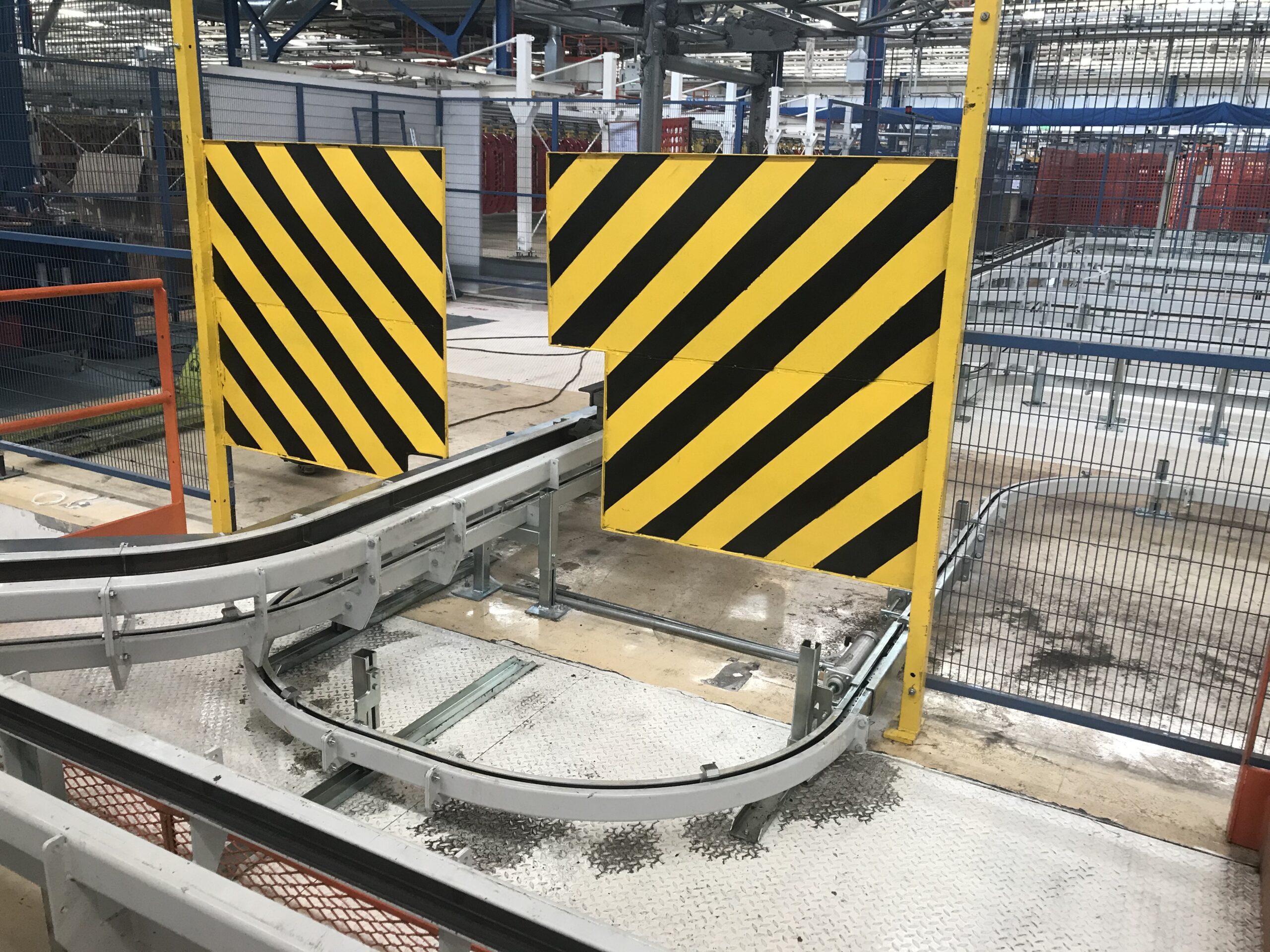 Binari curvi con barriera di sicurezza giallo-nera all’interno di un impianto industriale.