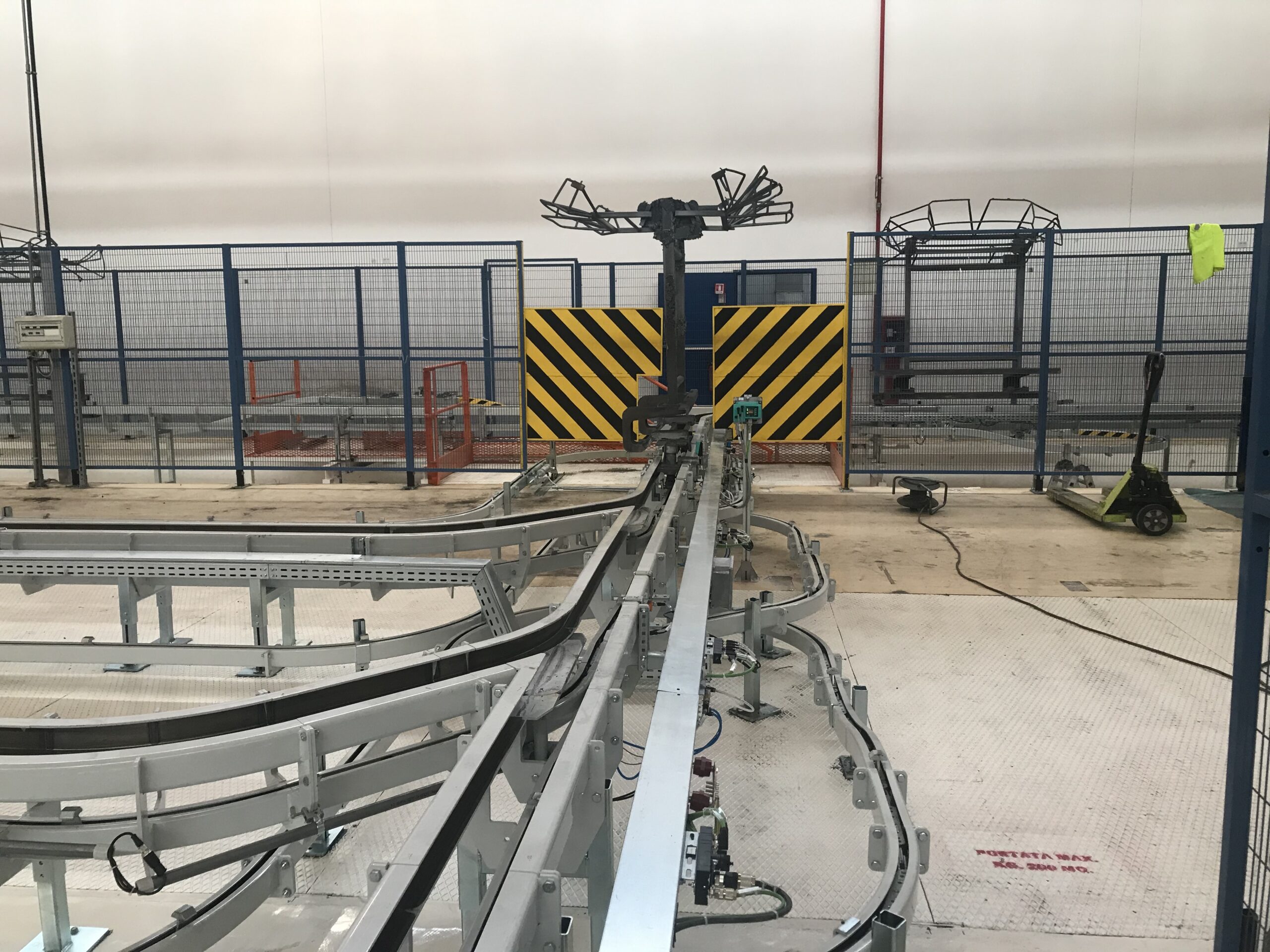 Sistema di trasporto industriale con binari metallici e recinzioni protettive blu.