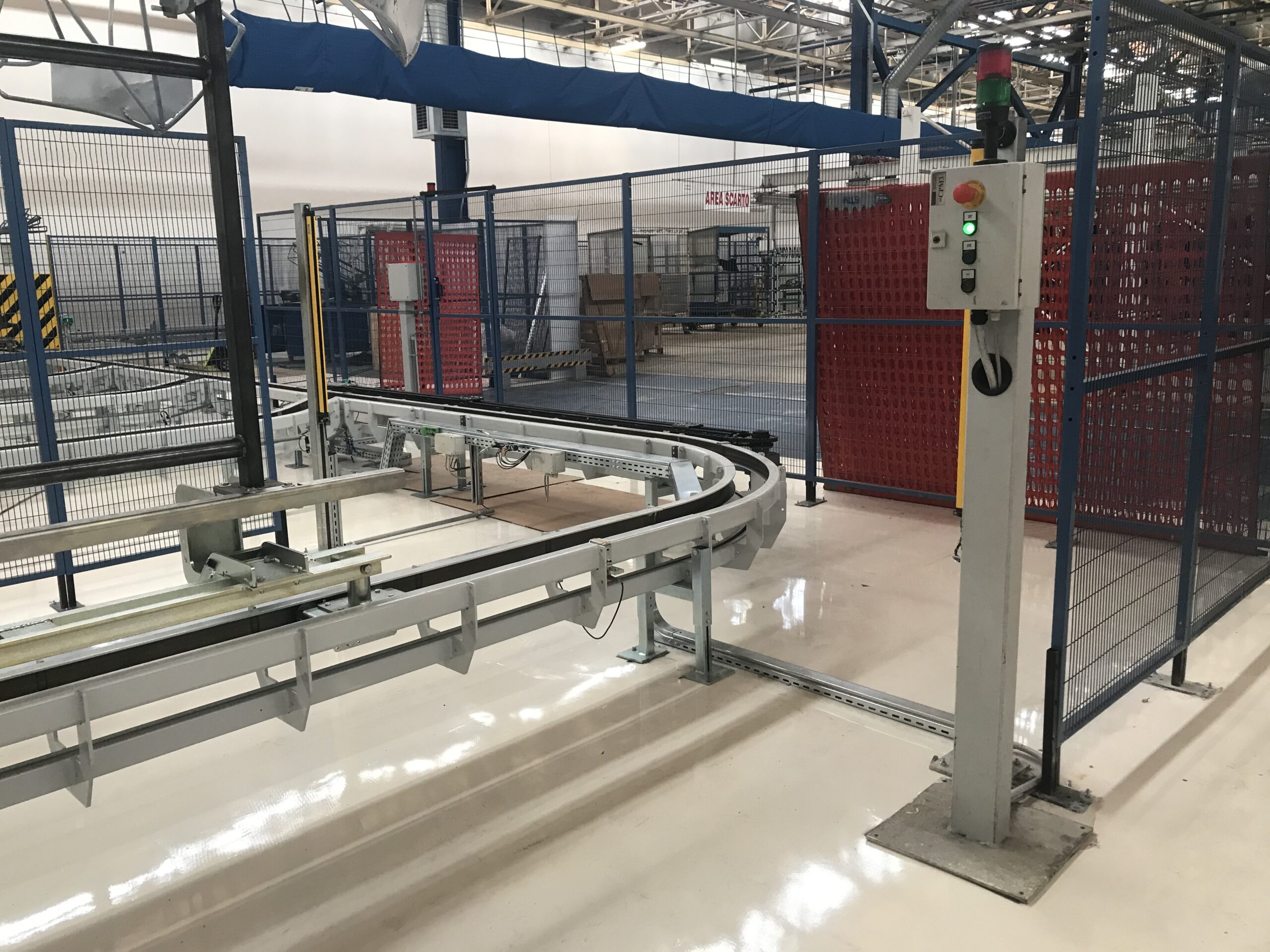 Vista di un impianto industriale con binari metallici, pulsantiera di comando e recinzione di sicurezza.