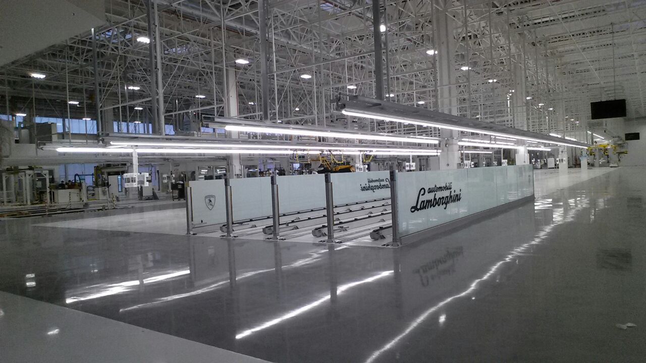 Impianto di trasporto Lamborghini con sistema su rotaie multiple, area delimitata da pannelli protettivi in vetro e design ottimizzato per produzioni di lusso.