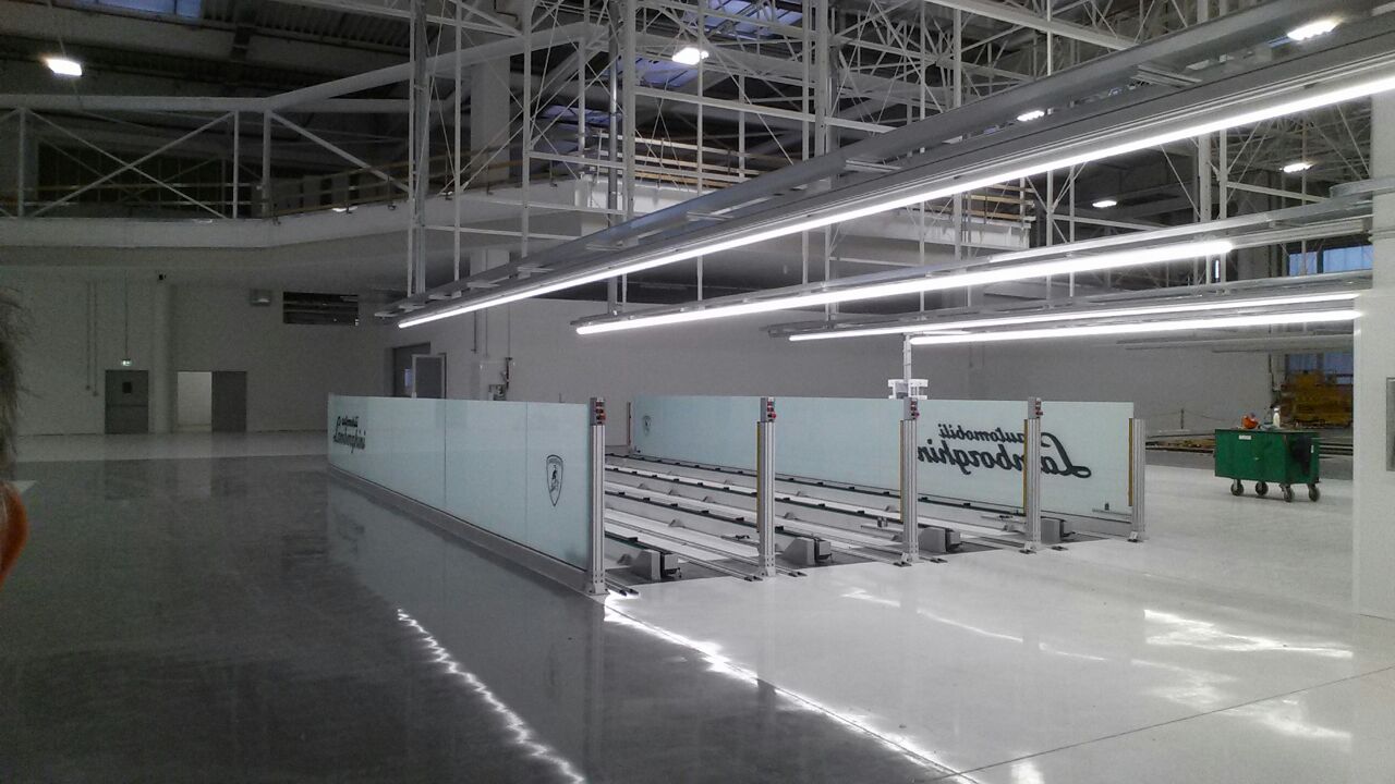 Impianto di trasporto Lamborghini con sistema su rotaie multiple, area delimitata da pannelli protettivi in vetro e design ottimizzato per produzioni di lusso.