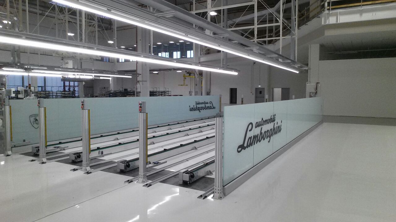 Linea di movimentazione interna Lamborghini, con guide parallele integrate e pannelli in vetro serigrafati, ideale per ambienti produttivi di alta gamma.