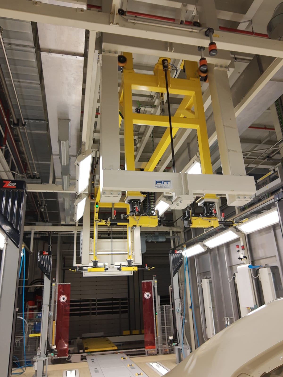 Impianto industriale con struttura gialla sospesa per il sollevamento e la movimentazione di carrozzerie auto.