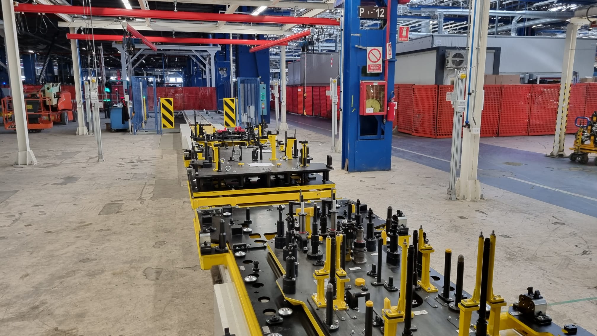 Attrezzature di produzione su carrelli gialli, con sistemi di fissaggio e controllo qualità per componenti industriali.